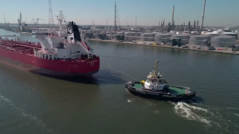 A harbour tug assisting a large vessel in an industrial port